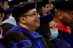Graduation ceremony with academic regalia and diverse graduates wearing face masks.