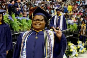 Graduation graduate smiling in cap and gown at ceremony, celebrating achievement and success.