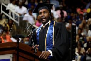 Graduation speaker in cap and gown delivering speech at ceremony.