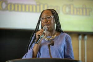 Empowered woman speaking at a conference with a microphone and presentation background.