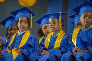 Graduation ceremony with children in blue caps and gowns, celebrating academic achievement.