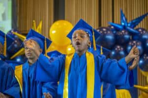 Graduation children in blue caps and gowns celebrating achievement at school ceremony.