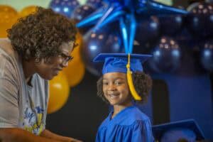 Happy young girl in graduation cap and gown smiling at her teacher during a celebration.