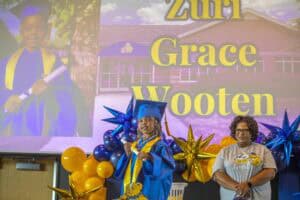 Brightly dressed graduate with cap and gown at graduation ceremony, colorful balloons, and a large s.