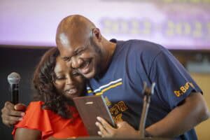 A woman and a man sharing a joyful moment while looking at a smartphone together at a public event.