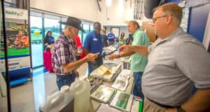 A man in a plaid shirt and cowboy hat purchasing items at a booth during an event.