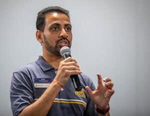 Advocate speaking at a conference, holding a microphone, wearing a navy polo with a name tag.