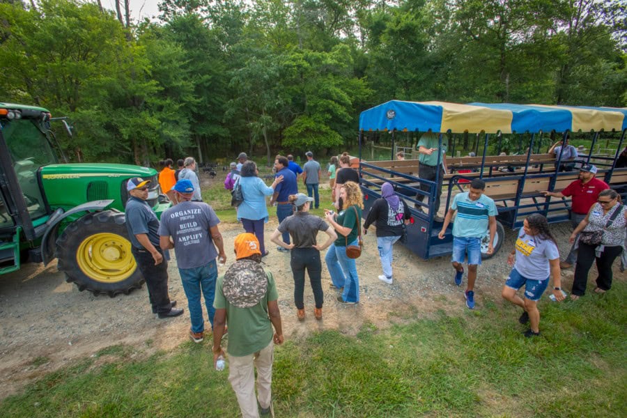 Community gathering around a tractor and trailer in a green outdoor setting.