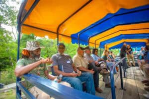 People sitting on a covered outdoor train ride at a park or zoo, enjoying the scenic view and relaxi.