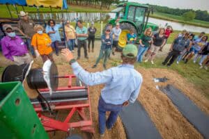 Agricultural demonstration with a group of people outdoors near a tractor and water body.