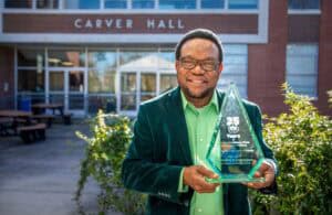 Celebrating 25 Years: Man holding an award outside Carver Hall, smiling for the camera.