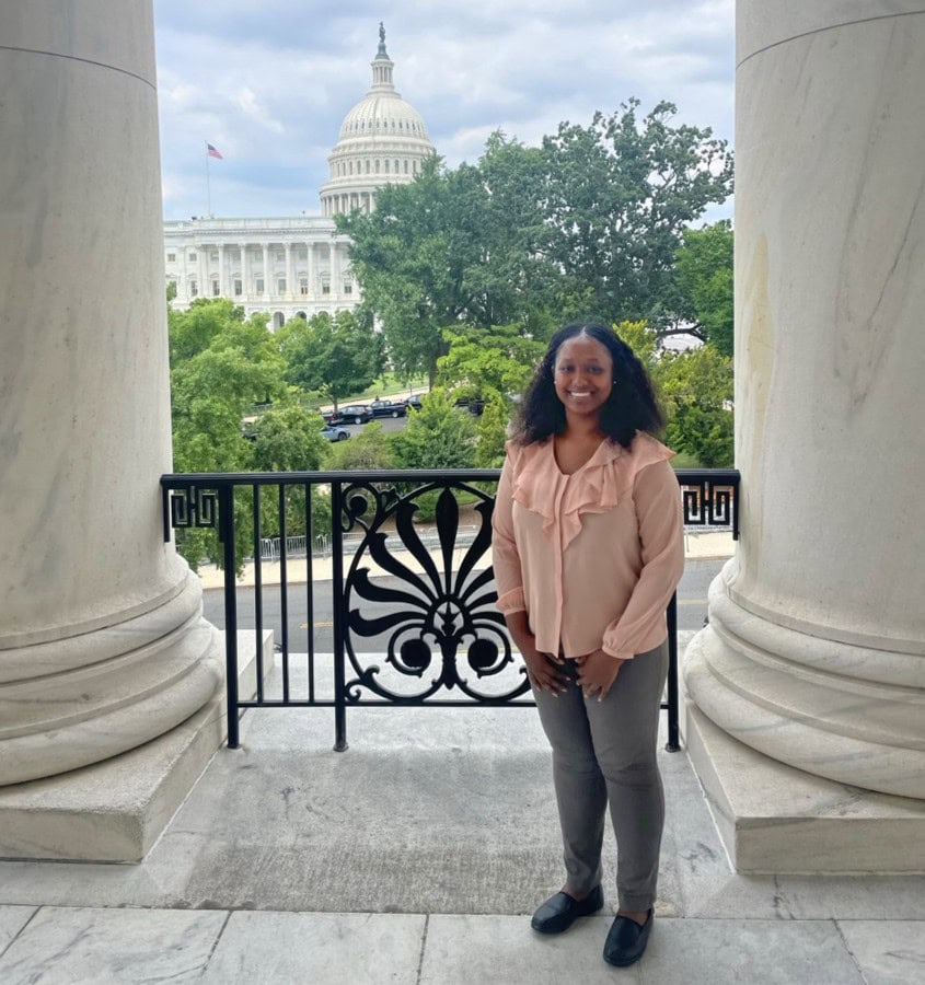 Woman standing on Capitol Hill balcony with U.S. Capitol in background.
