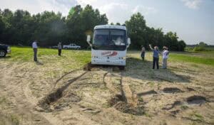 Bus stuck in muddy field with people inspecting, outdoor rural scene.