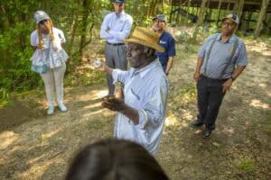 Community leader speaking to a group in a forest setting during daytime.
