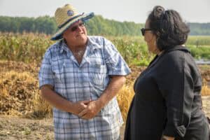 Older man and woman having a conversation outdoors in a rural setting, possibly discussing farming o.