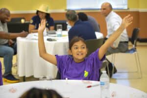 A girl raising her hands during a group activity or discussion at a community event.