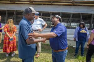Community leaders engaging in a handshake outdoors at a CAES News event.