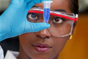 A scientist examining a test tube with a blue liquid in a laboratory setting.