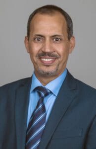 A man in a business suit smiling, professional headshot for corporate or news profile.