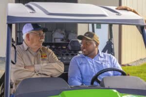 Two men having a conversation inside a green golf cart outdoors.
