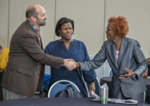 Shaking hands at a professional meeting with diverse women in business attire.
