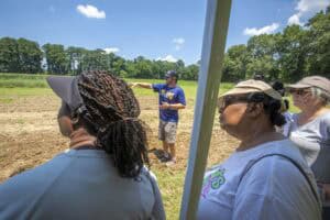Community outdoor event with diverse group listening to a speaker in a field.