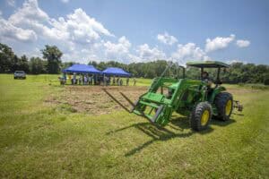 Green tractor with front loader working on a grassy field under a blue sky with clouds.