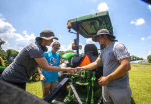 Plantation demonstration with people inspecting and operating agricultural machinery outdoors on a s.