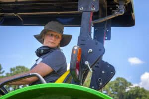 Woman operating agricultural machinery outdoors under blue sky.