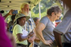 Engaged diverse group of people attending outdoor event, listening attentively and taking notes.