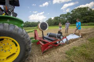 Agricultural workers using equipment in a field during daytime for crop planting or soil preparation.