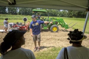 Planting demonstration with tractor and instructor at outdoor agricultural event.