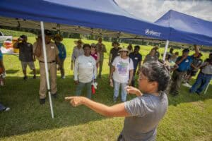 Community outdoor event with diverse group under blue canopy in sunny weather.