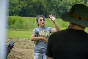 A woman speaking outdoors during a discussion or interview in a rural setting.