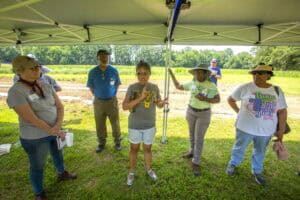 Community group discussing agricultural or environmental topics outdoors under a canopy.