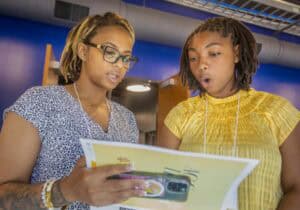 Two women reviewing documents and a smartphone in an office setting.