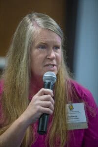 A woman speaking into a microphone at a conference or event.
