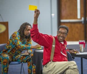 Accessible voting at a conference with diverse participants, including a man raising a yellow voting.