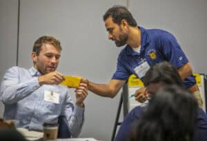 A man handing a yellow card to another man at a professional event or conference.