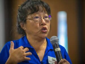 An SEO-friendly ALT tag: Woman speaking at a conference with microphone, wearing blue shirt and glas.