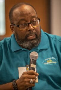 Engaged man speaking into microphone at conference, wearing blue polo with CAES logo.