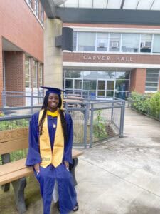 Graduating student in cap and gown outside Carver Hall at CAES News campus.