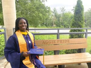 Graduation graduate girl in cap and gown holding diploma outdoors on campus.