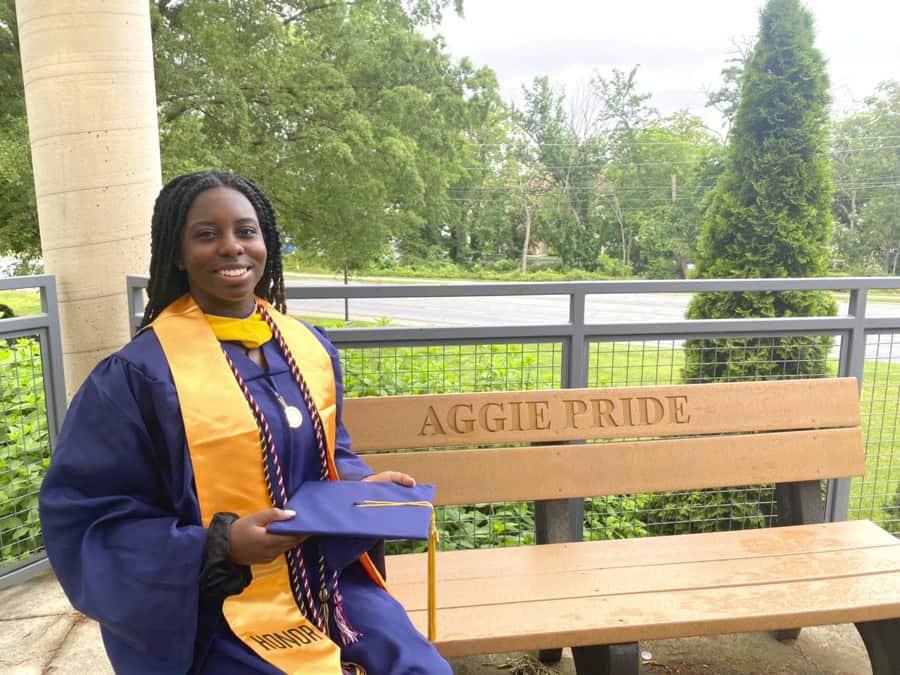 Graduation graduate girl in cap and gown holding diploma outdoors on campus.