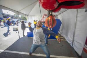 A man posing with a boxing punching bag at an outdoor event under a white tent.