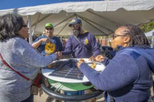 Solar energy event with diverse group of people exchanging handshake and conversation outdoors.