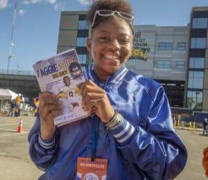 Celebrating Aggie Pride at the university football game with a smiling student holding a program.