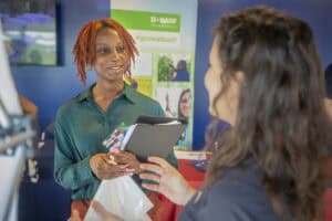 A woman with red dreadlocks smiling and holding a tablet during a professional event.