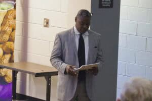 A man in a gray suit reading a document at an indoor event.
