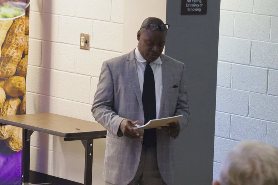 A man in a gray suit reading a document at an indoor event.